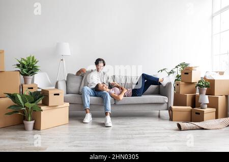 Une jeune femme et un gars caucasiens satisfaits font une pause, se détendant sur un canapé à l'intérieur de la chambre parmi des boîtes avec des effets personnels Banque D'Images