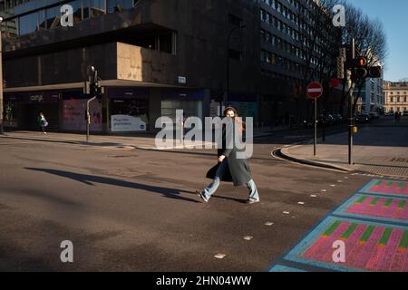 Une femme aux cheveux longs traverse Tottenham court Road, Londres, lors d'une journée d'hiver lumineuse mais froide. Banque D'Images