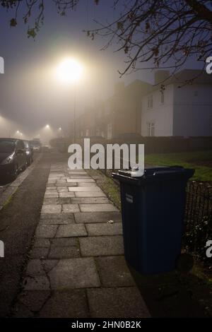 Poubelle à roulettes sous les feux de la rue lors d'une matinée humide et brumeuse dans le nord de Londres, au Royaume-Uni Banque D'Images