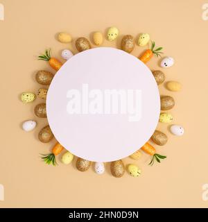Carte papier pour Pâques avec petits œufs blancs et dorés jaunes et carottes autour du papier sur fond beige pastel. Pose à plat Banque D'Images