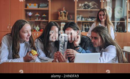 Des filles d'école travaillent ensemble en classe avec un ordinateur portable et manger des pommes. Banque D'Images