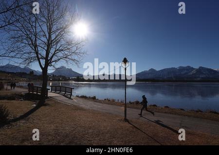 13 février 2022, Bavière, Füssen: Un jogging court au soleil sur la promenade côtière du lac Hopfensee, situé au bord des Alpes. Photo : Karl-Josef Hildenbrand/dpa Banque D'Images