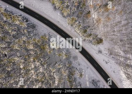 Vue aérienne de la route d'hiver dans la forêt enneigée. Tir de drone capturé par le dessus Banque D'Images
