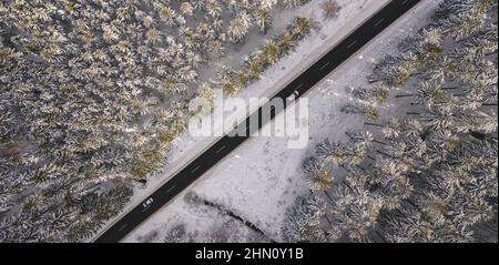Vue aérienne de la forêt enneigée avec une route et une voiture. Capturé par le dessus avec un drone Banque D'Images
