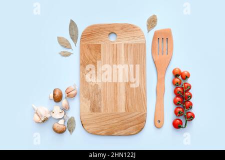 Planche à découper et spatule en bois avec épices et légumes sur fond bleu clair, vue de dessus. Banque D'Images