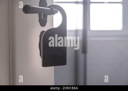 Le cintre de la chambre d'hôtel est vide. Étiquette noire sur la vue rapprochée du bouton de porte rétro ouverte. Porte en bois blanc, intérieur flou Banque D'Images