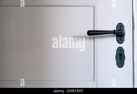 Vue rapprochée de la poignée et de la serrure de porte intérieure. Poignée de porte et serrure en métal noir rétro sur porte à panneaux blancs fermée avec décoration, espace de copie Banque D'Images