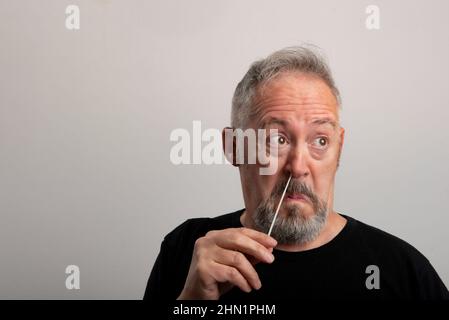 homme d'âge moyen avec cheveux gris et barbe utilisant le coronavirus (covid-19) kit d'auto-test rapide (atk) à la maison avec un coton-tige nasal Banque D'Images