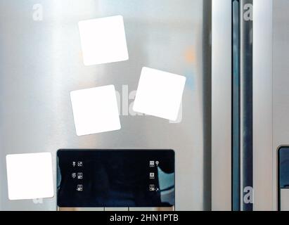 Quatre notes vierges en papier blanc sont fixées sur la porte grise du réfrigérateur Banque D'Images