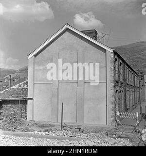 La construction de Central Road (de gauche à droite en premier plan), Port Talbot, West Glamourgan, pays de Galles, Royaume-Uni à la fin de 1950s – ici, la nouvelle route avait exigé la démolition de maisons en terrasses. Un nouveau mur d'extrémité en béton (ou une extrémité en pignon avec contreplaque) a été ajouté au 16, rue Penrhyn. Central Road était l'une des principales voies d'accès aux aciéries. Finalement, la route principale vers les travaux a été via Cefn Gwrgan Road. Cependant, ces deux routes d'accès ont été coupées par la construction de la voie de contournement de Harbour Way en 2013 – une photographie vintage 1950s/60s. Banque D'Images