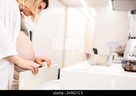 Femme enceinte blonde blanche cuisinant dans la cuisine à la maison Banque D'Images