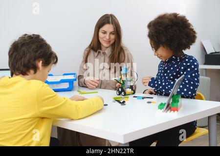 Des enfants multiethniques à la LEÇON STEM construire un robot dans une salle de classe avec une femme enseignante les enfants font un modèle de bras électronique à l'école de science moderne Banque D'Images