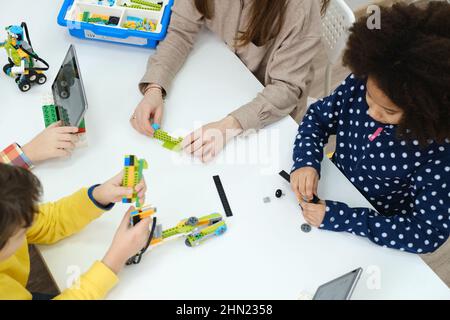 Des enfants multiethniques à la LEÇON STEM construire un robot dans une salle de classe avec une femme enseignante les enfants font un modèle de bras électronique à l'école de science moderne Banque D'Images