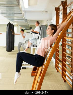 Une jeune femme se lève les jambes sur les barres murales de la salle de sport Banque D'Images