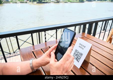 Mains d'une femme méconnaissable scannant un code QR avec un smartphone pour accéder à un menu de restaurant ; utilisation de la technologie sans contact dans la vie quotidienne. Sortie Banque D'Images