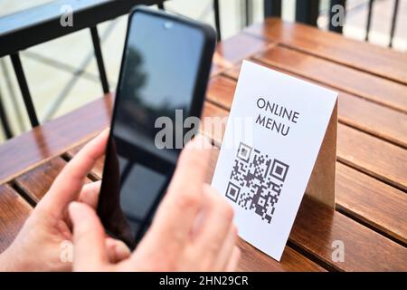 Mains d'une femme méconnaissable scannant un code QR avec un smartphone pour accéder à un menu de restaurant ; utilisation de la technologie sans contact dans la vie quotidienne. Banque D'Images