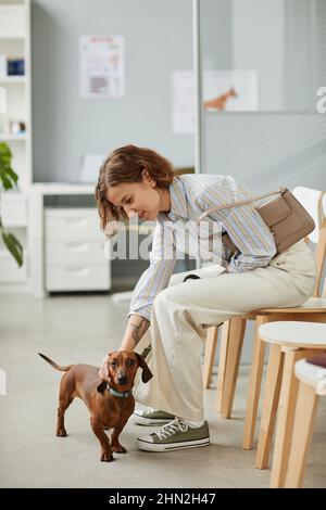 Jeune propriétaire d'animal de compagnie choquant son chien de dachshund en s'asseyant dans des cliniques vétérinaires et se pliant sur un animal domestique mignon Banque D'Images