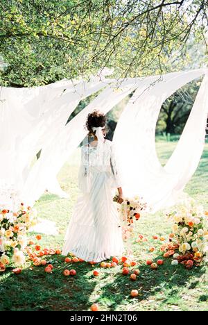 Femme avec un bouquet de fleurs se dresse devant des rideaux blancs dans le jardin. Vue arrière Banque D'Images