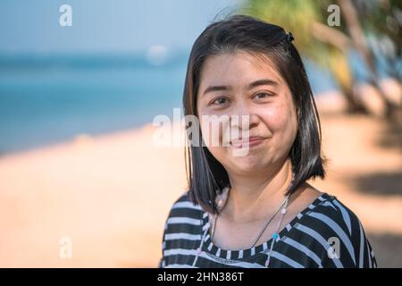 Portrait d'une femme asiatique d'âge moyen sur la plage, visage heureux avec visage souriant, peau naturelle sans maquillage, taches de taches, imperfections de la peau. Flou b Banque D'Images