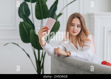 Jeune femme faisant le selfie, étant photographiée sur un téléphone intelligent. Blogueur d'influenceur pour créer du contenu pour les médias sociaux. Concept de style de vie à l'intérieur. Banque D'Images