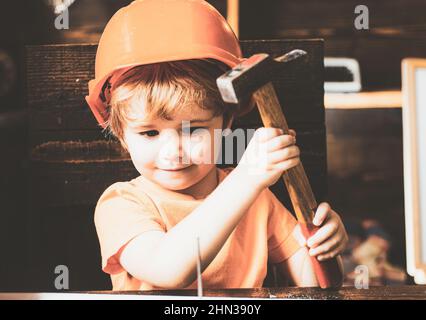 Un petit garçon avec un marteau fait des réparations. L'enfant participe activement au processus fait à la main. Banque D'Images