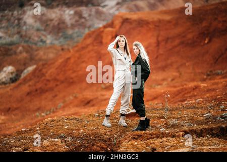 Filles dans un lieu post-apocalyptique, une carrière avec la terre rouge et des pierres dans les vêtements de travail Banque D'Images