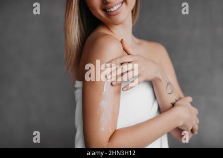 Gros plan ou femme appliquant de la lotion hydratante pour le corps sur l'épaule, en utilisant de la crème nourrissante pour la peau Banque D'Images