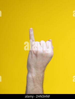 Main d'homme verticale bien entretenue avec paume dans le poing et petit doigt droit sur fond jaune. Symbole japonais signe de la femme, de la femme ou de la langue Banque D'Images