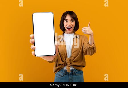 Jolie femme millénaire tenant un smartphone avec écran vide et gestuelle Banque D'Images