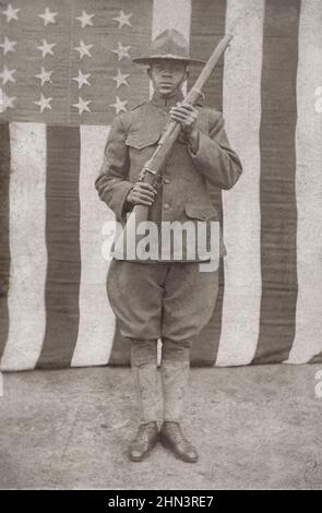 USA pendant la première Guerre mondiale. Soldat américain africain en uniforme et chapeau de campagne avec fusil devant le drapeau américain. 1917-1918 Banque D'Images