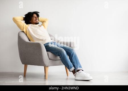 Confort domestique. Portrait de Happy Black Man relaxant dans fauteuil à la maison Banque D'Images