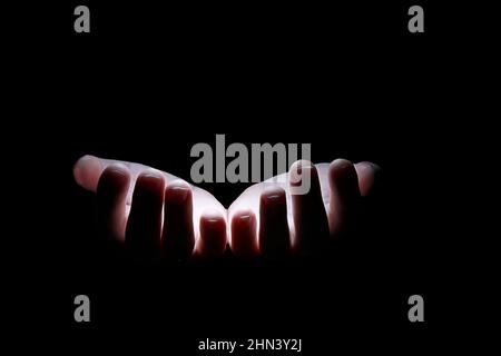 Deux paumes d'une personne dans l'obscurité sont illuminées par la lumière. Deux mains humaines sur fond noir en lumière blanche. Gros plan de l'isolation. Banque D'Images
