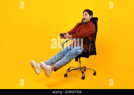 Joueur Guy jouant jeu vidéo tenant le contrôleur assis, fond jaune Banque D'Images