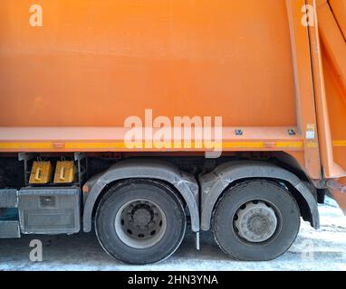 Fragment d'une grande machine d'élimination des déchets. Camion à ordures orange. Essieux arrière d'un chariot. Bunker orange ou benne à ordures. Arrière-plan orange Banque D'Images