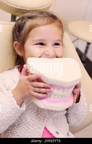 Baby Girl sitting in fauteuil dentaire avec mâchoire artificielle dans les mains Banque D'Images