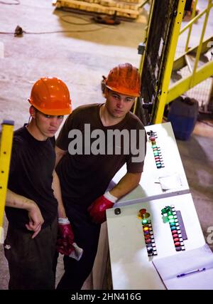 Temirtau, Kazakhstan - 09 juin 2012 : usine de fabrication de traverses de béton NORD Prom NS. Deux jeunes travailleurs et console d'équipement. Banque D'Images