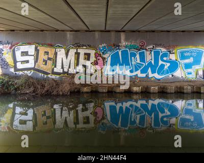 Graffiti coloré sous un pont routier au-dessus d'un canal, avec des reflets dans l'eau; Northampton, Royaume-Uni Banque D'Images