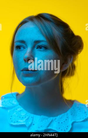 Gros plan de la jeune jolie fille avec des taches de rousseur posant isolé sur fond jaune au néon. Concept d'émotions, expressions faciales Banque D'Images