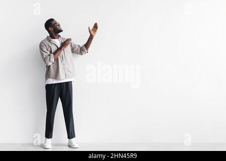 Pleine longueur de beau jeune homme noir pointant à l'espace vide pour votre conception d'annonce contre le mur blanc de studio Banque D'Images