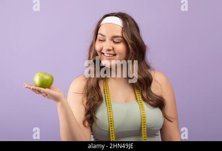 Joyeuse millénaire européenne plus taille femme avec mètre-ruban de sport tient la pomme verte à portée de main Banque D'Images