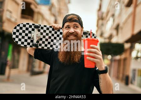 Jeune patineur irlandais tenant du skate et buvant du soda à la ville. Banque D'Images