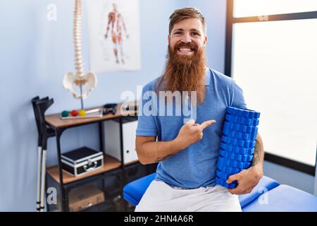 REDHEAD homme avec la longue barbe tenant le rouleau en mousse à la clinique médicale souriant heureux de pointer avec la main et le doigt Banque D'Images