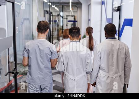 Vue arrière de plusieurs jeunes travailleurs médicaux interculturels en blouse de laboratoire et uniforme discutant des points de travail en mouvement Banque D'Images