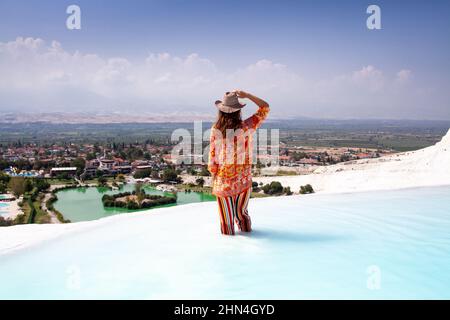 Jeune femme en chapeau de paille séjour dans la piscine de travertin rempli d'eau turquoise et regardant le paysage à couper le souffle de la terrasse à Pamukkale. Transvert naturel Banque D'Images