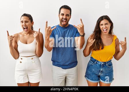 Groupe de jeunes hispaniques se tenant sur un fond isolé criant avec une expression folle faisant le symbole du rock avec les mains vers le haut. Star de la musique. Heavy mus Banque D'Images