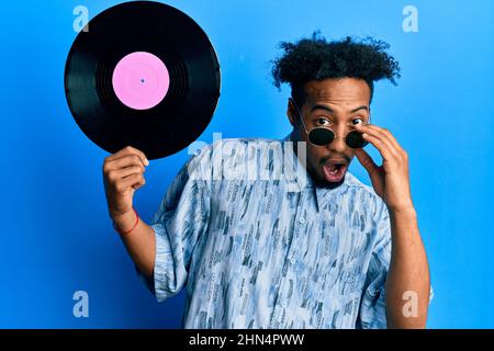 Jeune africain américain avec la barbe tenant disque de vinyle peur et stupéfait avec la bouche ouverte pour la surprise, incrédulité visage Banque D'Images