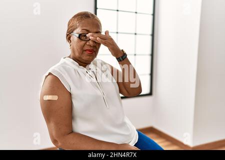 Femme hispanique mature qui obtient le vaccin montrant le bras avec l'aide de bande couvrant les yeux avec la main, regardant grave et triste. sightless, cachette et rejet conc Banque D'Images