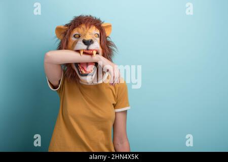 Jeune femme en masque de lion mordent sa propre main, isolée sur fond bleu avec l'espace de copie. Banque D'Images