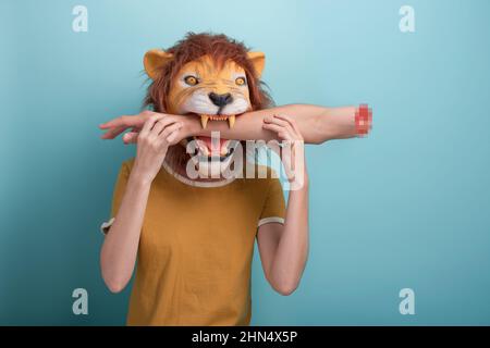 Jeune femme en masque de lion avec mordu de la main dans sa bouche, isolée sur fond bleu. Banque D'Images