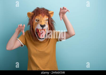 Jeune femme dans le masque de lion faisant des gestes effrayants d'attaque avec les mains, isolé sur fond bleu avec l'espace de copie. Banque D'Images